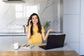 oung cheerful happy woman indoors at home at the kitchen using laptop computer talking by mobile phone Royalty Free Stock Photo