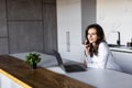 Photo of a young cheerful woman indoors at home at the kitchen using laptop computer talking by mobile phone Royalty Free Stock Photo