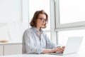 Photo of young concentrated woman in striped shirt using laptop