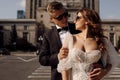 Photo of young couple, bride and groom in sunglasses, like special agents in wedding dress. there is city landscape in background