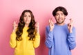 Photo of young couple worried nervous crossed fingers wish luck success isolated over pink color background