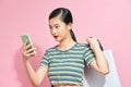Photo of young excited cheerful woman holding shopping bags isolated over pink background using mobile phone Royalty Free Stock Photo