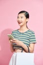 Photo of young excited cheerful woman holding shopping bags isolated over pink background using mobile phone Royalty Free Stock Photo