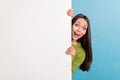 Photo of young excited girl hiding behind white wall advertise blank card isolated over blue color background