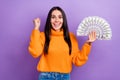 Photo of young funky overjoyed woman brunette hair wear orange sweater fist up hold much money win lottery isolated on Royalty Free Stock Photo