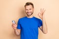 Photo of young guy use mobile show fingers okey symbol recommend promo perfect isolated over beige color background