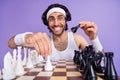 Photo of young happy cheerful smiling funky geek nerd man in glasses playing chess isolated on violet color background Royalty Free Stock Photo