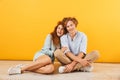 Photo of young happy couple man and woman 20s smiling and hugging while sitting on floor together, isolated over yellow background Royalty Free Stock Photo