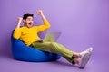 Photo of young happy crazy excited smiling man sit armchair with laptop raise fists in victory  on violet color Royalty Free Stock Photo