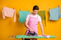 Photo of young happy handsome cheerful positive focused man ironing washed clothes isolated on yellow color background