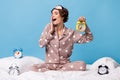 Photo of young happy positive smiling funky girl yawning sit on bed surrounded by clocks  on blue color Royalty Free Stock Photo