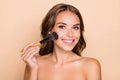 Photo of young happy smiling beautiful woman doing contouring apply blush on cheeks isolated on beige color background Royalty Free Stock Photo