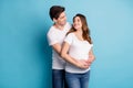 Photo of young happy smiling couple look at each other husband embrace wife belly isolated on blue color background Royalty Free Stock Photo