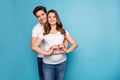 Photo of young happy smiling couple pregnant wife and husband showing heart on belly isolated on blue color background Royalty Free Stock Photo