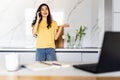 Photo of a young happy woman indoors at home at the kitchen using laptop computer talking by mobile phone Royalty Free Stock Photo