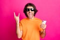 Photo of young mad guy hold telephone open mouth show horns wear orange t-shirt sunglass isolated pink color background Royalty Free Stock Photo