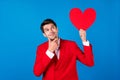 Photo of young man happy positive smile hand touch chin think look paper card heart valentine day  over blue Royalty Free Stock Photo