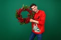 Photo of young man happy positive smile hold christmas wreath evergreen tree decoration new year isolated over green Royalty Free Stock Photo