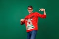 Photo of young man happy positive smile point finger decor reindeer jumper eyeglasses costume isolated over green color