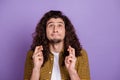 Photo of young man look empty space crossed fingers pray wish luck over purple color background