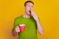 Photo of young man sleepy early morning yawn drink hot coffee cup isolated over yellow color background Royalty Free Stock Photo