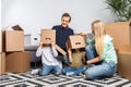 Photo of young married couple with indulging children sitting on floor among cardboard boxes