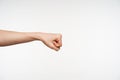 Photo of young pretty female`s hand being raised while clenching fingers into fist and moving it ahead, posing against white Royalty Free Stock Photo