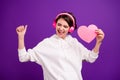 Photo of young smiling good mood funky girl listen music in headset hold pink paper heart isolated on purple color Royalty Free Stock Photo