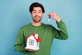 Photo of young smiling handsome man holding little house new key relocation isolated on blue color background