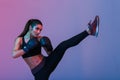 Photo of young sportswoman 20s in tracksuit and black boxing gloves fighting and kickboxing on training, isolated over dark