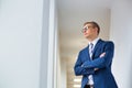 Young thoughtful businessman standing with arms crossed looking away in office corridor Royalty Free Stock Photo