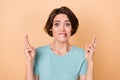 Photo of young woman anxious bite lisps crossed fingers pleading isolated over beige color background