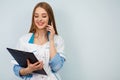 Photo of a young woman doctor posing  over white wall background holding clipboard talking by mobile phone Royalty Free Stock Photo