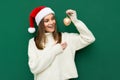 Photo of young woman happy positive smile hold hands balls decor christmas santa hat isolated over green color background Royalty Free Stock Photo