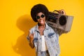 Photo of young woman wear casual jeans clothes holding boombox showing hard rock sign tongue isolated yellow color Royalty Free Stock Photo