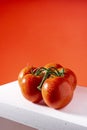 Photograph of a branch of five natural tomatoes on a white table and a red background