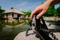 Photograph male hand handling an old vintage camera on tripod in front of water pond with landmark japanese house and Royalty Free Stock Photo