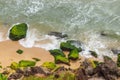 Photograph shows a beautiful sea beach where waves are crashing in to white foam on rocks which are covered with green algae Royalty Free Stock Photo