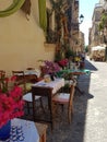 Photograph of a small Sicilian restaurant opening onto a narrow street whose tables are nicely decorated and colorful