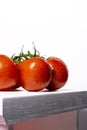 Photograph of three wet red natural tomatoes on a white bench and a white background.The photo has copy space Royalty Free Stock Photo