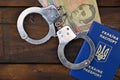 A photograph of a Ukrainian foreign passport, a certain amount of Ukrainian money and police handcuffs. Concept of illegal earnin