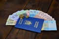 A photograph of a Ukrainian passport and a certain amount of Ukrainian money on a wooden surface. The concept of making money for