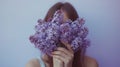 A photograph of a woman holding a bouquet of violet lilacs that cover her face, set against a lavender background. Royalty Free Stock Photo