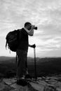 Photographer with big mirror camera on neck and backpack stay on peak of rock. Hilly landscape, fresh green color in valley. Royalty Free Stock Photo