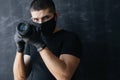 Photographer in a black mask, a T-shirt and gloves, holds the camera in his hands on a dark background. Concept Photo business