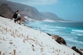 Photographer with camera enjoying quaint moment in scenic coastal landscape of sand dunes and volcanic cliffs. Baia Das Royalty Free Stock Photo