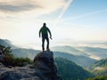 Photographer with camera in hands on top of mountain. Hiker climbed on peak of rock above foggy valley