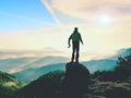 Photographer with camera in hands on top of mountain. Hiker climbed on peak of rock above foggy valley