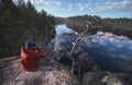 A photographer with a camera sits on the granite shore of a picturesque forest lake. Mirror surface of the lake Royalty Free Stock Photo