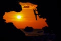 Photographer climbing rock in the cave near the beach at red sky sunset Royalty Free Stock Photo